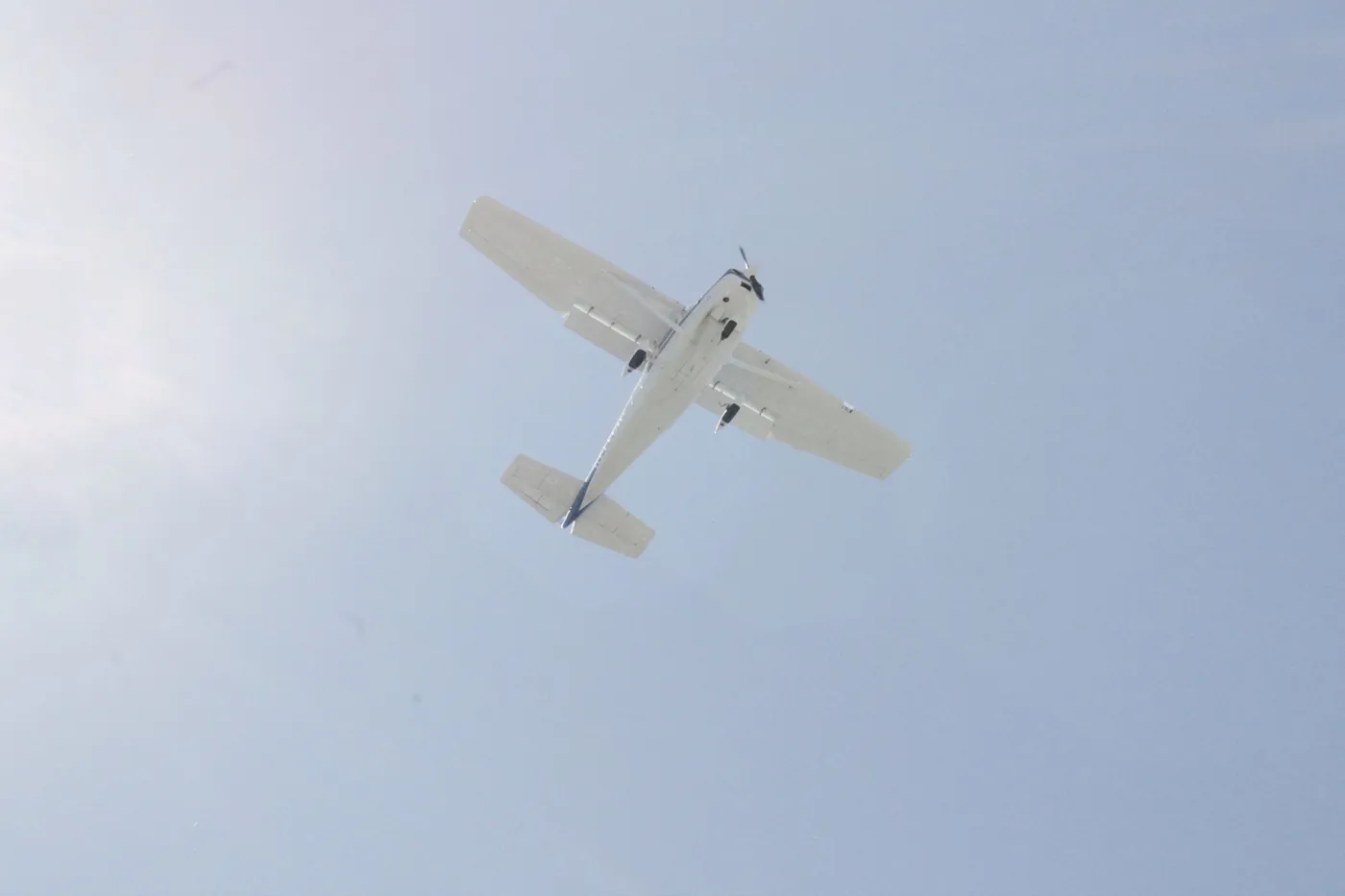 A small white single-engine plane seen from below against a pale blue sky